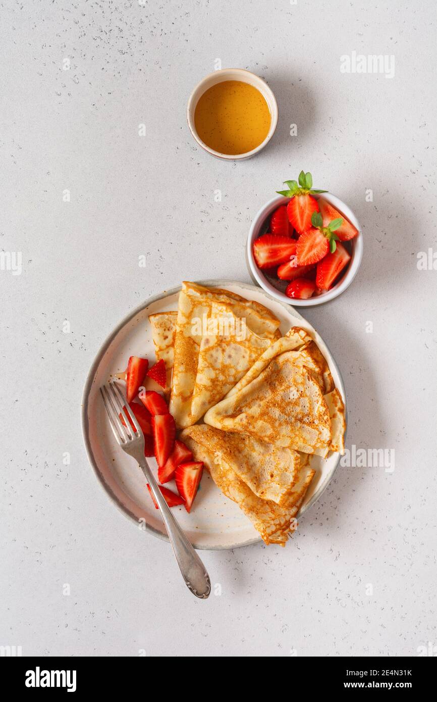 Traditional dish for holiday Maslenitsa. Thin crepes pancakes with honey, fresh strawberry and ingredients for making breakfast. Top view Stock Photo