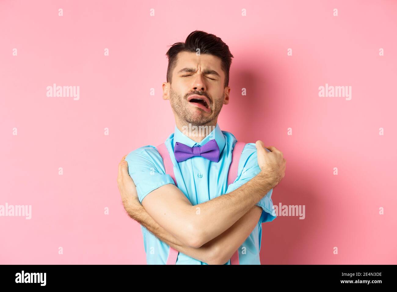 Crying guy hugging himself, feeling sad and lonely, standing unhappy on pink background Stock Photo