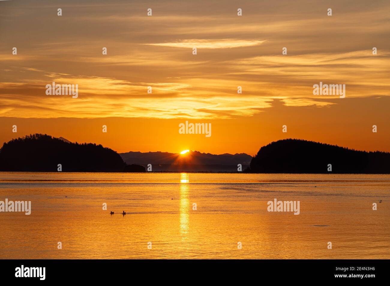 Dramatic sun rising between two hills with water in the foreground