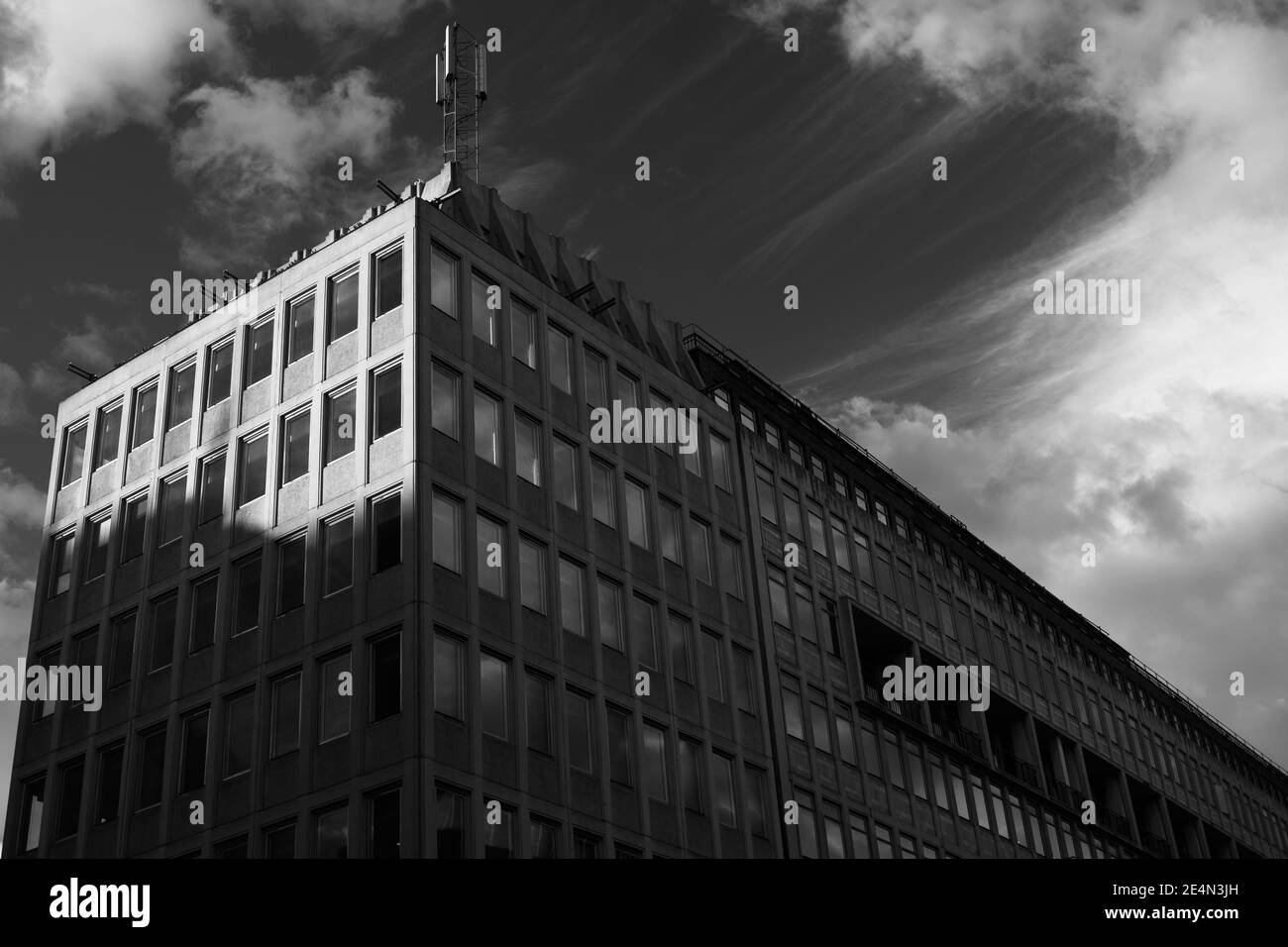 Black and white monochrome image looking up at 20th century 1960s concrete office building. Mobile cell phone mast on roof. Sunny day with shadows cas Stock Photo