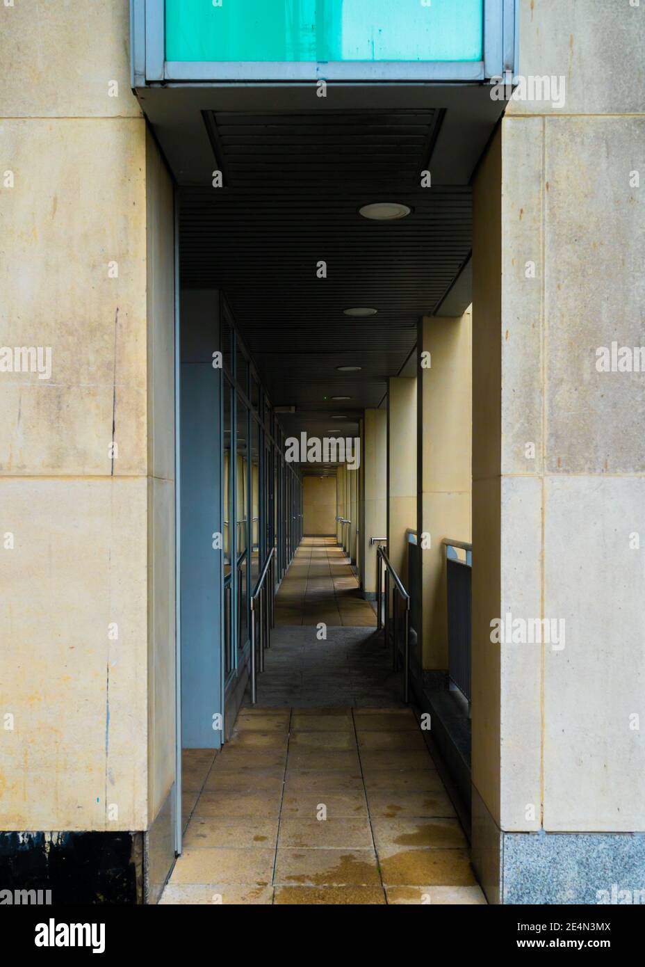 Covered, dimly lit pathway under modern apartments Stock Photo