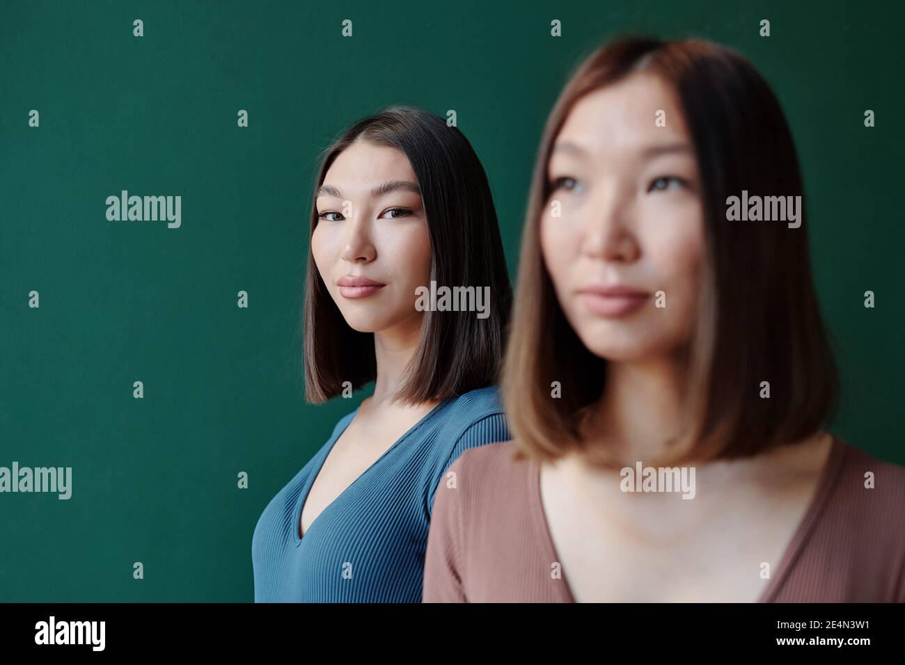 Young Brunette Female Of Asian Ethnicity With Natural Makeup Looking At You While Standing Behind Her Gorgeous Twin Sister In Studio Stock Photo Alamy