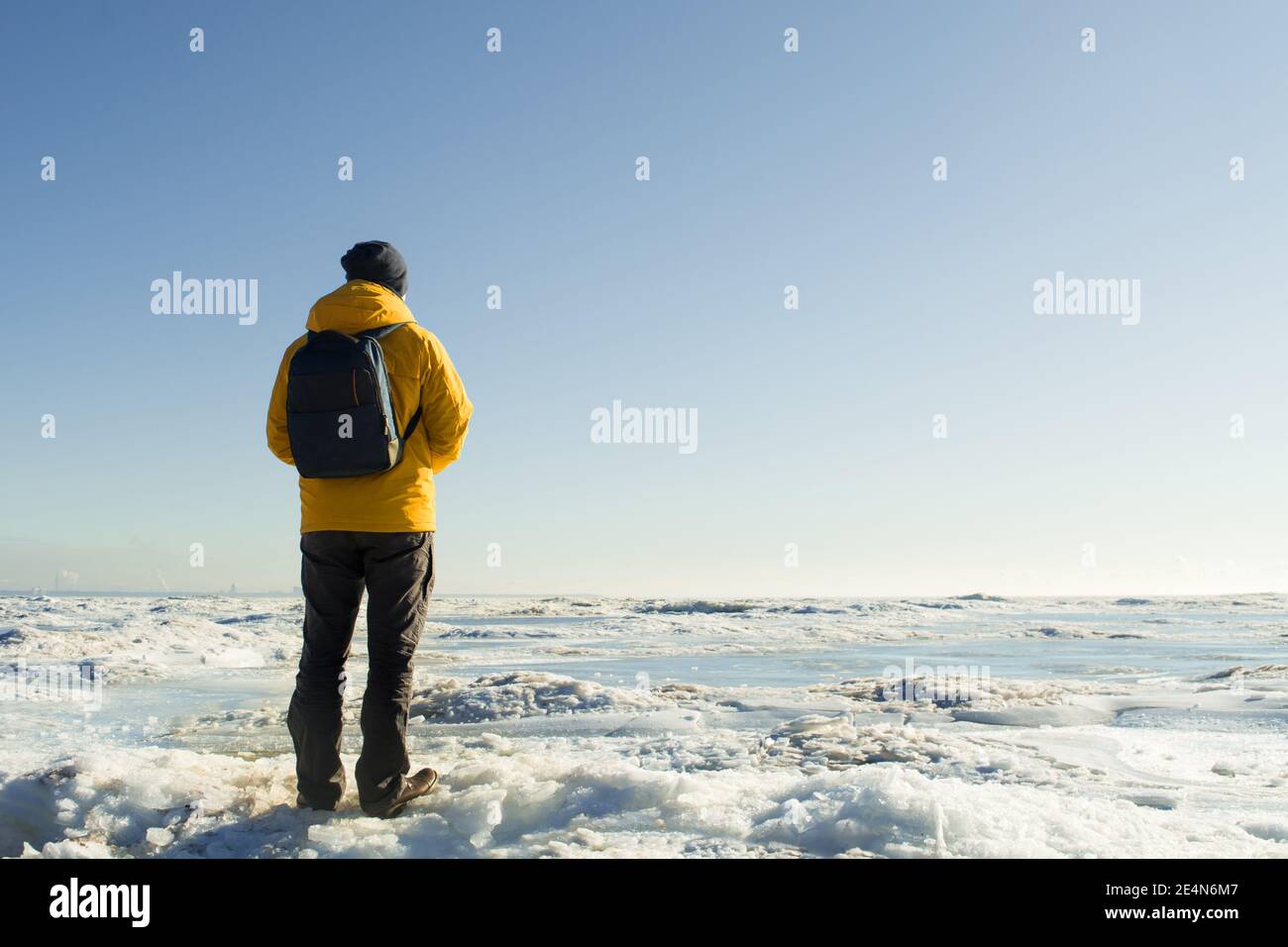 Faceless man in yellow raincoat with backpack standing and looking on frozen sea Stock Photo