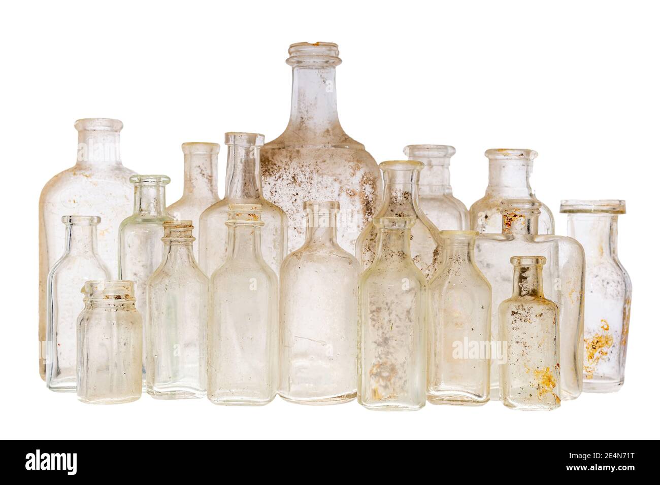 A collection of old antique bottles against a white background. There are 18 ancient bottles, and they are dirty. Focus on the front row. Stock Photo