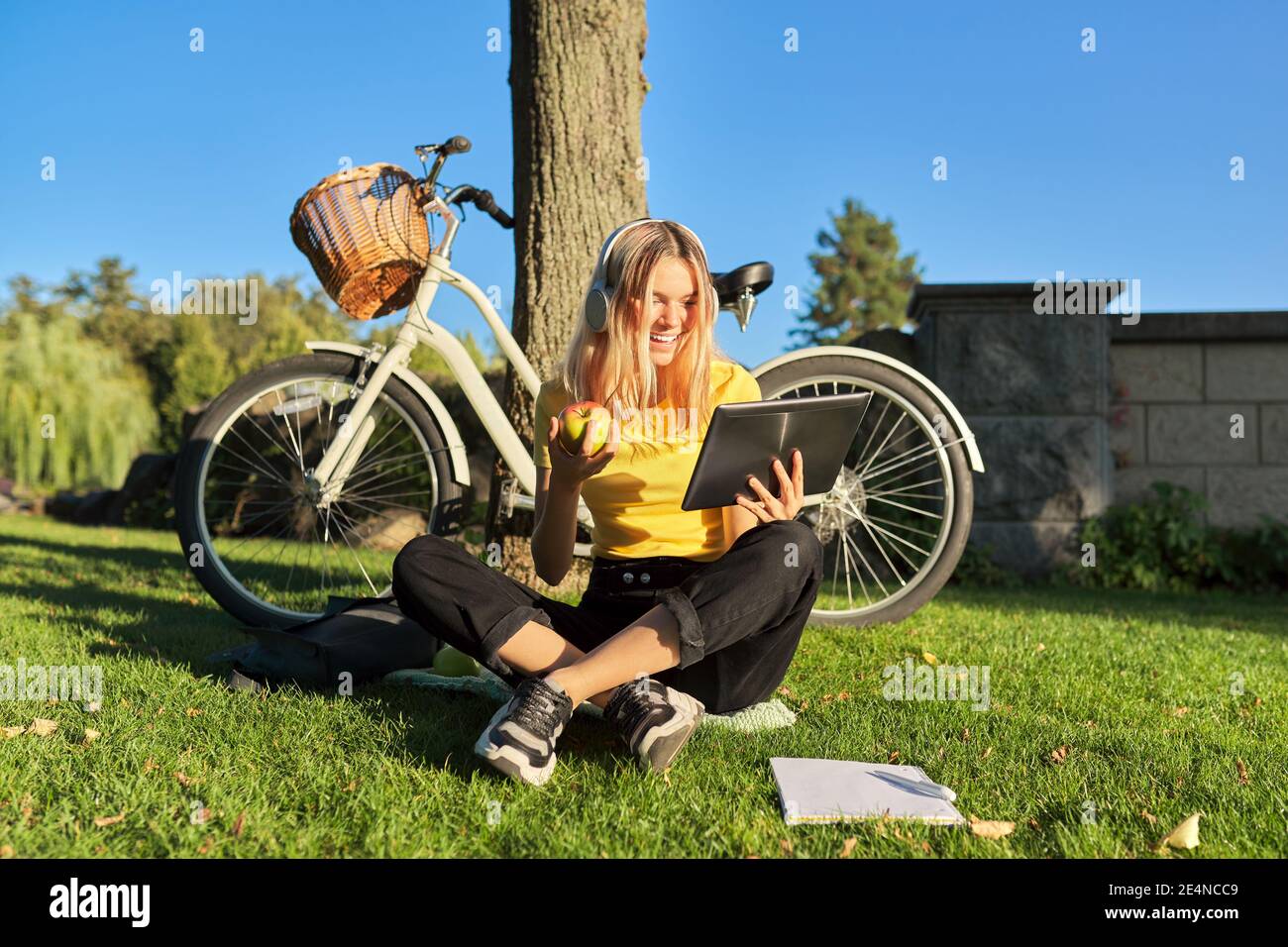 Female studentin in headphones looking at digital tablet screen talking sitting on grass Stock Photo