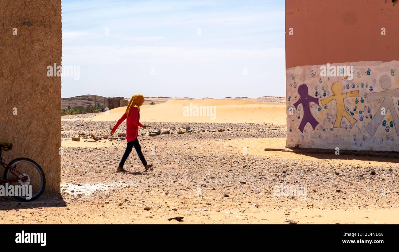 Moroccan girl runs between two school buildings in the Sahara desert in the summer Stock Photo