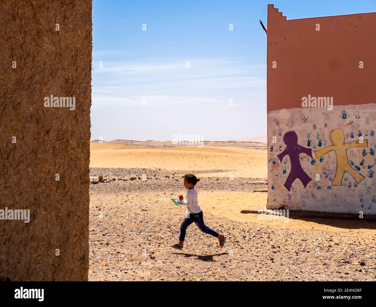 Moroccan girl runs between two school buildings in the Sahara desert in the summer Stock Photo