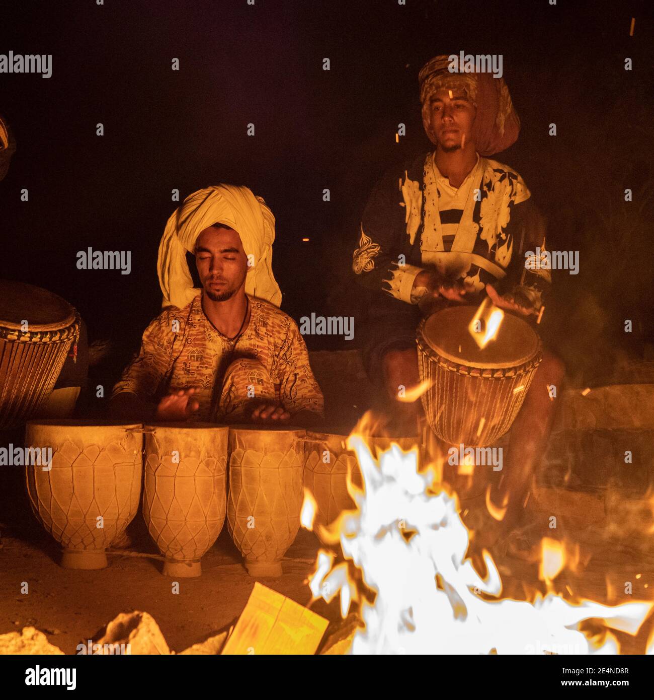 Two young turbaned musicians play their instruments by a campfire in the night Sahara desert. Stock Photo