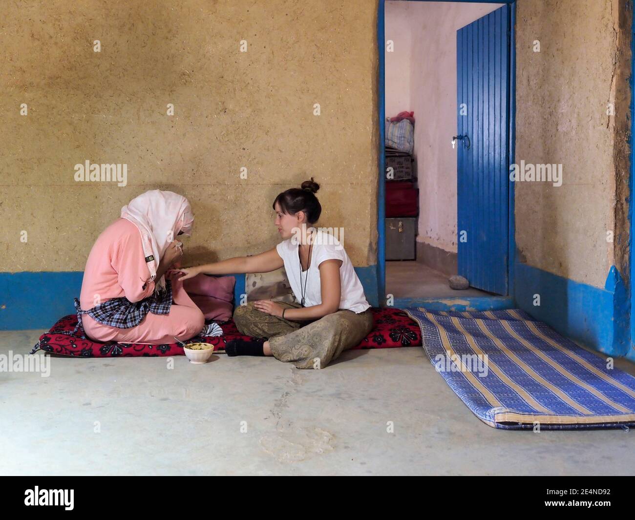 A young Moroccan girl paints the hands of a tourist sitting on the floor, with traditional henna. Stock Photo