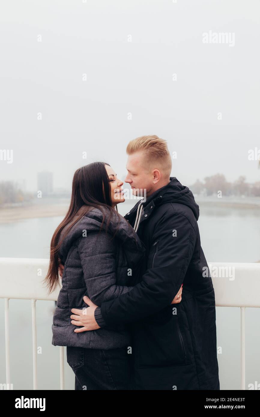 A young couple in warm clothes hugs and looks at each other against the background of a foggy landscape. High quality photo Stock Photo