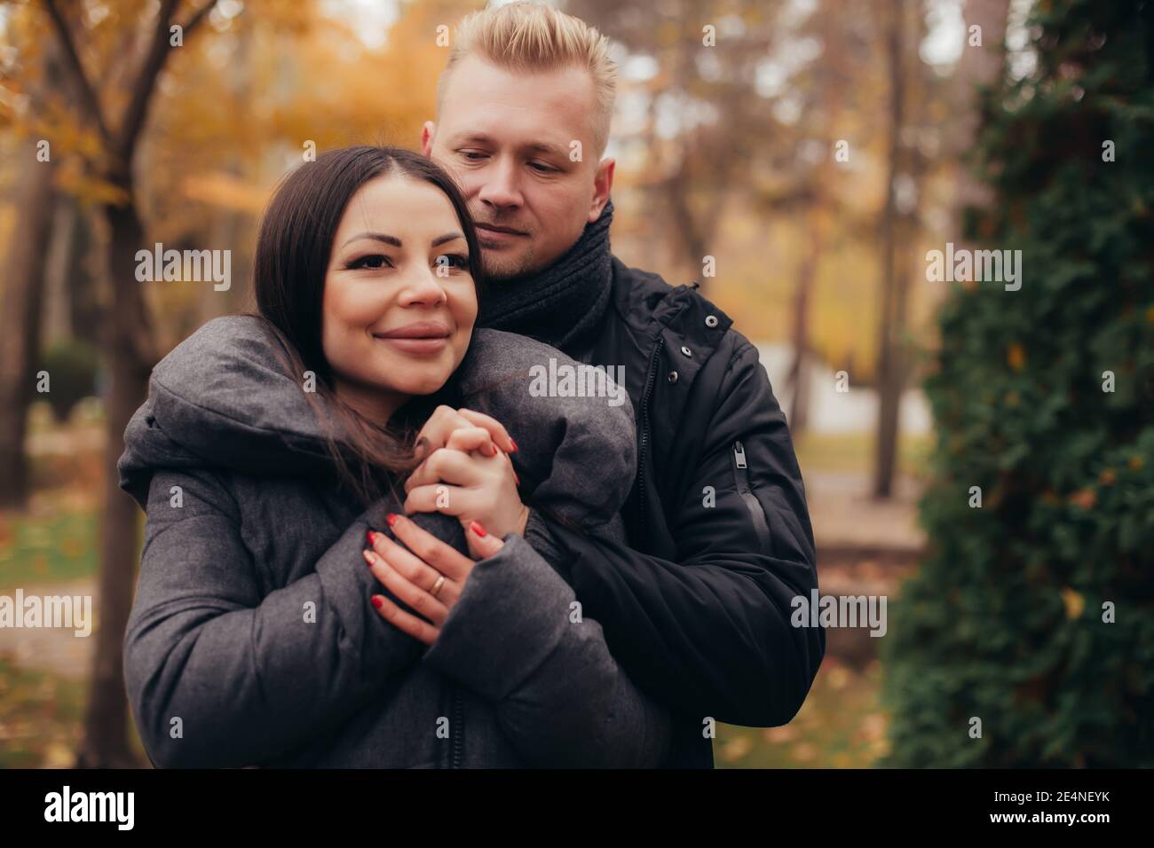 A man hugs and holds the hand of his girlfriend as she smiles in the cold weather in the autumn park. High quality photo Stock Photo