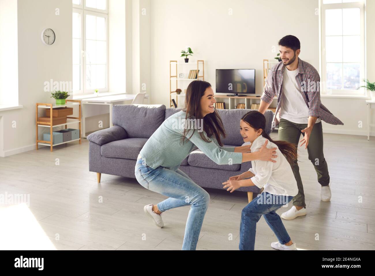 Playful mom, dad and daughter running around the room and fooling around at home during the weekend. Stock Photo