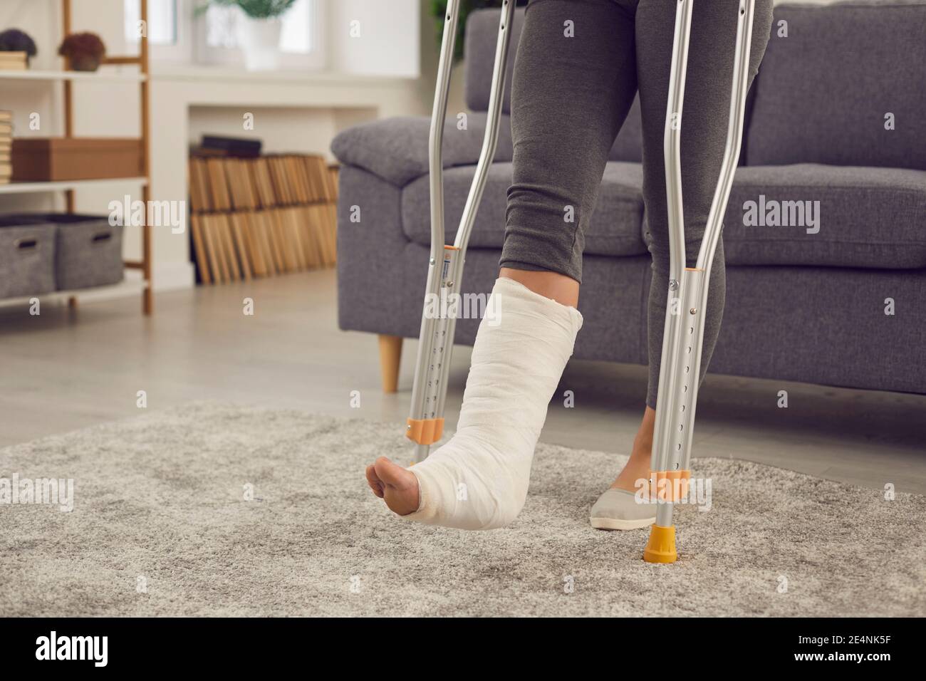 Person with broken leg in cast stands up from couch and walks with crutches at home Stock Photo