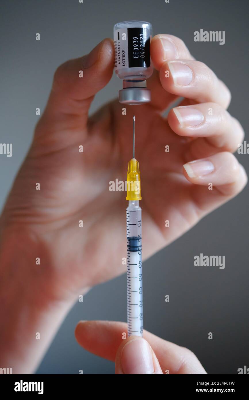 Genuine Pfizer-BioNTech COVID-19 Vaccine vial hold in hand with syringe needle next to it. Real vaccine photo. Selective focus. Stafford, United Kingd Stock Photo