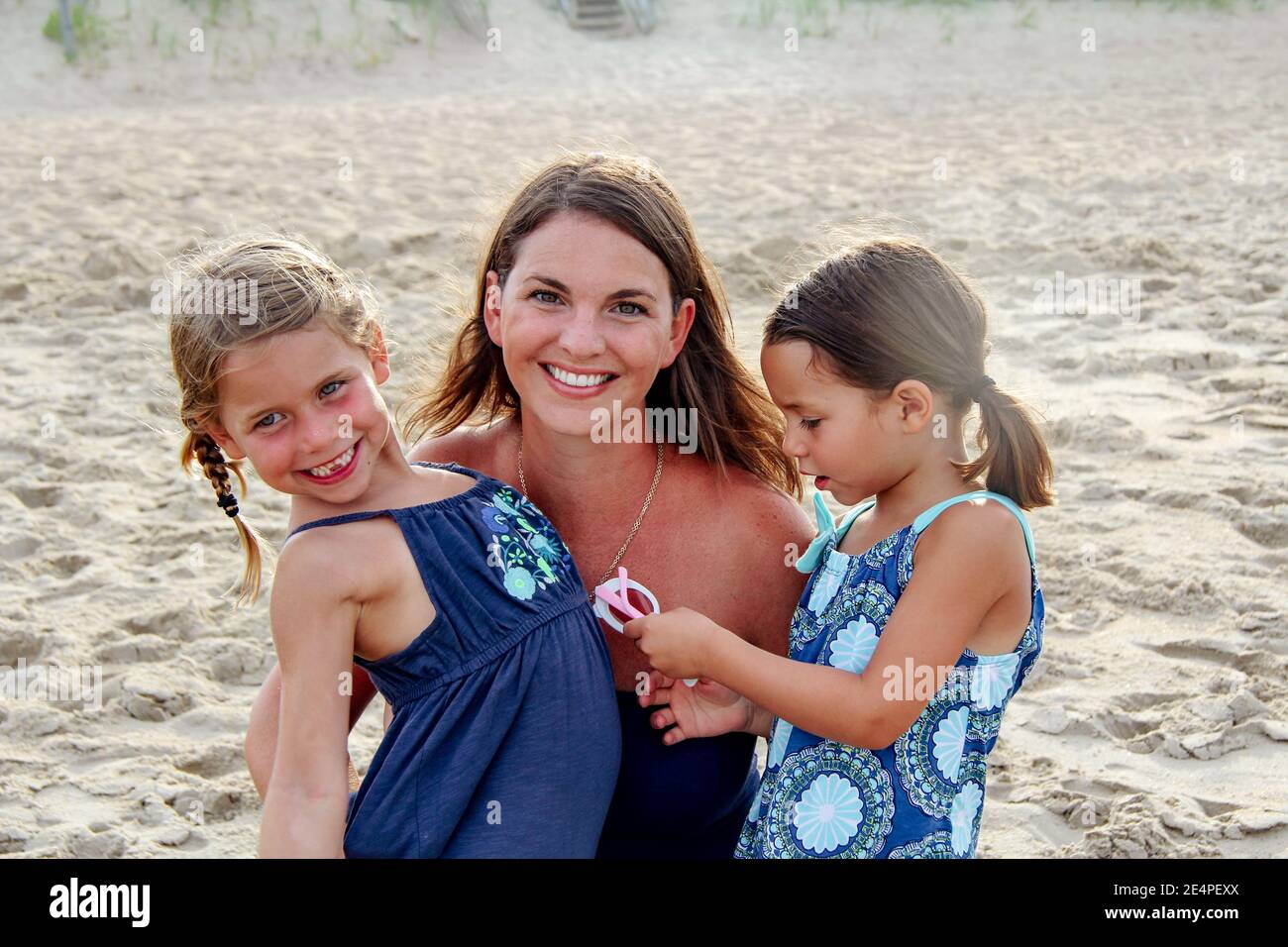 Brunette, smiley mother and two beautiful daughters spending quality time at a sandy beach Stock Photo