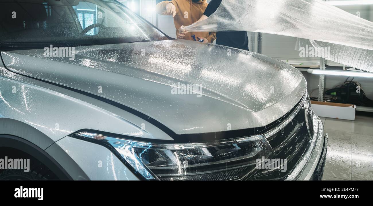 Process of installing of Paint Protection Film or PPF on new car in professional auto Detailing Center. Thin polyurethane film or polymer as protective skin from scratches and rock chips. Stock Photo
