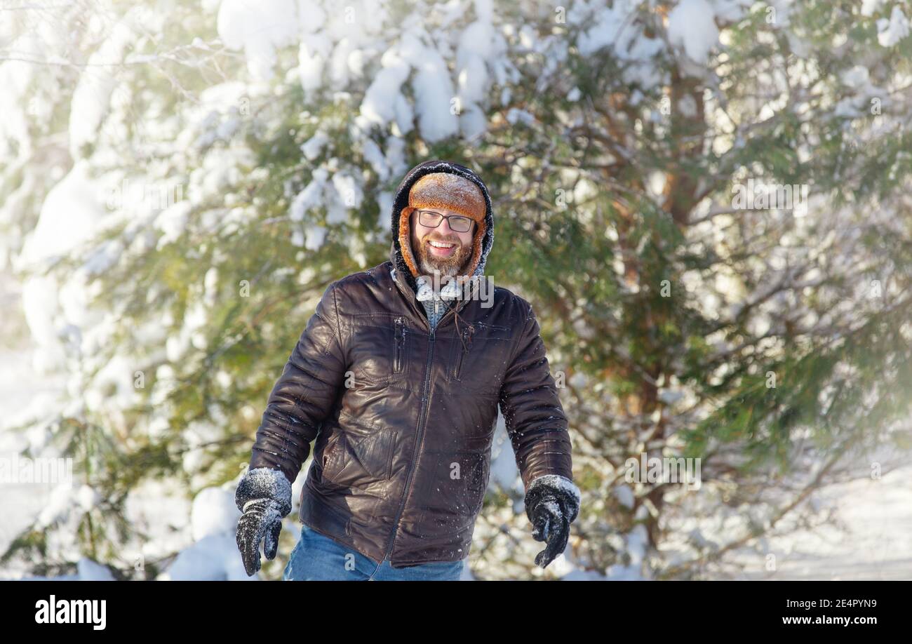 a man with a beard and mustache, wearing a fur hat and jacket, on a sunny day in a winter forest Stock Photo