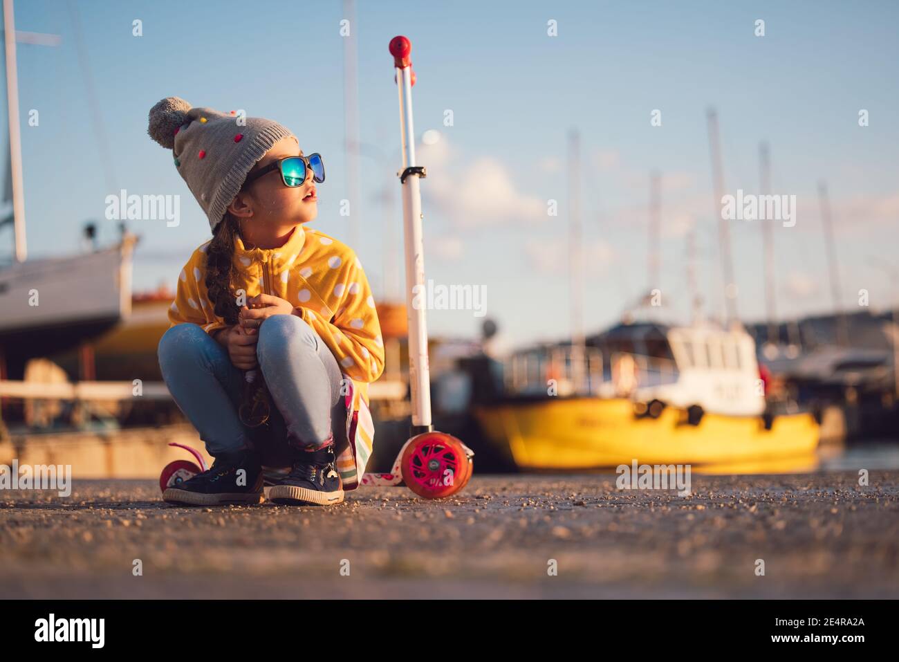 Little girl riding scooter outdoor near sea harbour Stock Photo