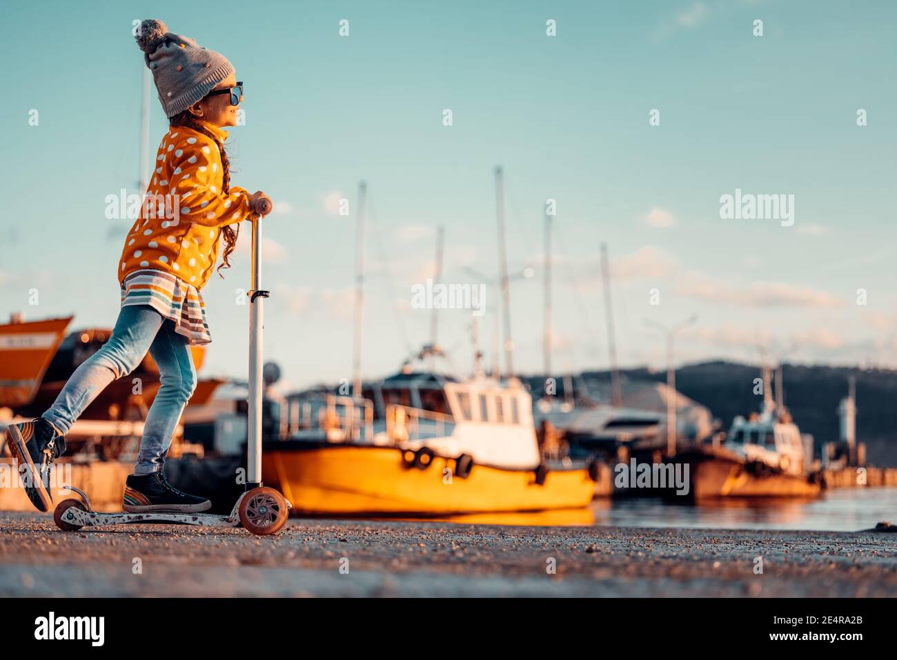 Little girl riding scooter outdoor near sea harbour Stock Photo