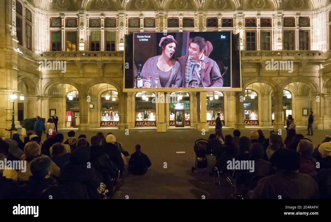 People sitting outside the Wiener Staatsoper or Vienna State Opera House view a performance for free on an outdoor screen Stock Photo