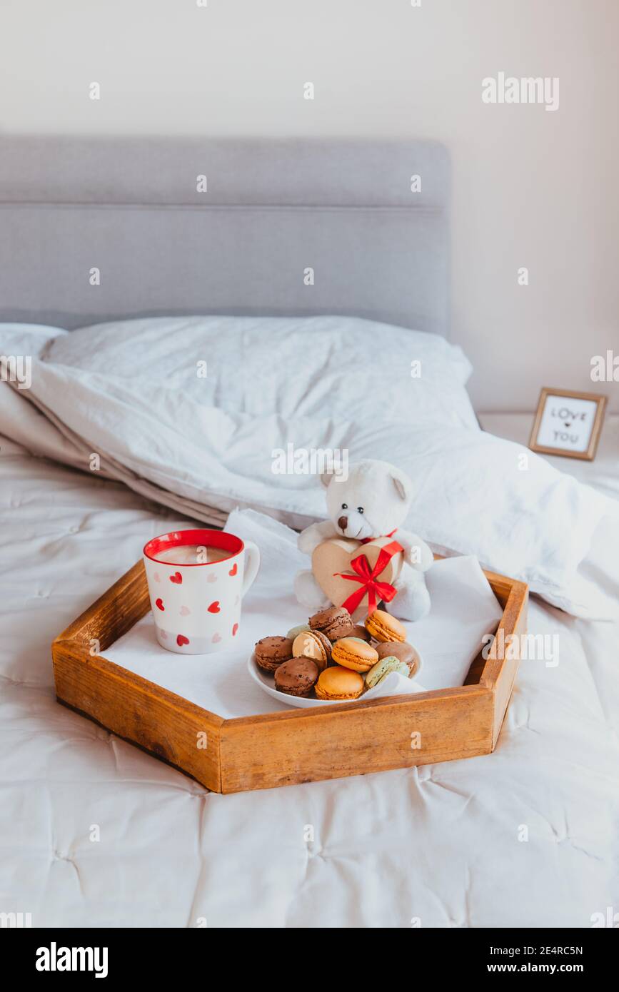 Valentine's day breakfast in bed for Lover. Teddy Bear with a heart-shaped gift box with red ribbon, a cup of coffee, and macaroons cookies on the Stock Photo