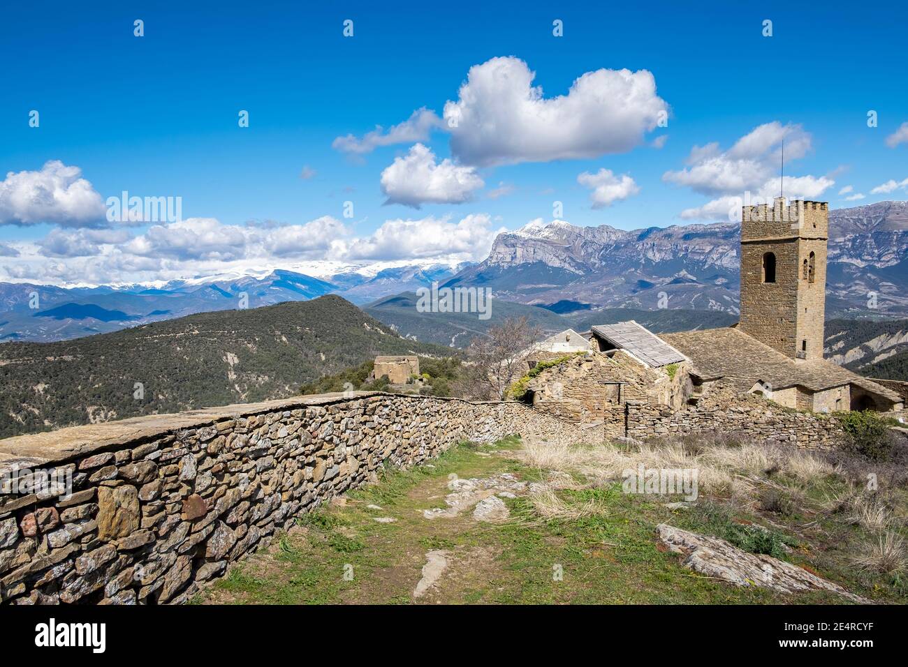 medieval walled village in ruins with a crenelated tower and snow-capped mountains in the background, walled enclosure of Muro de la Roda, La Fueva, S Stock Photo