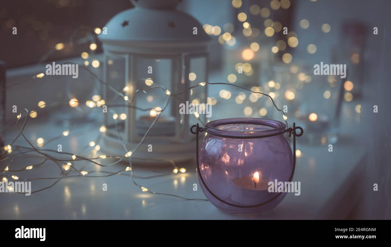 Closeup of burning tea candles in lantern and glasses on sill. Led