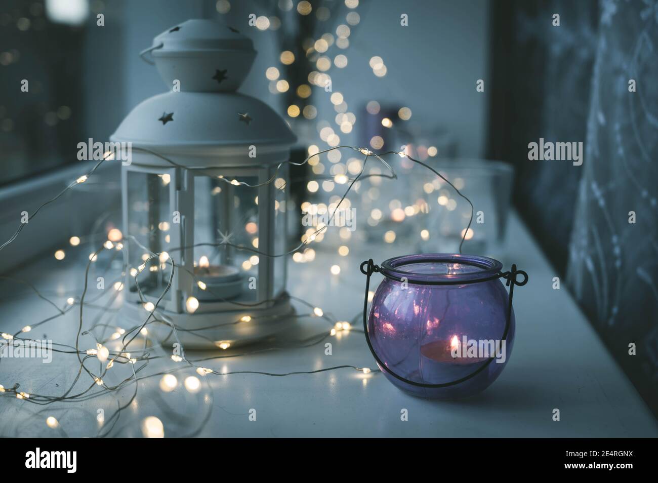 Closeup of burning tea candles in lantern and glasses on sill. Led