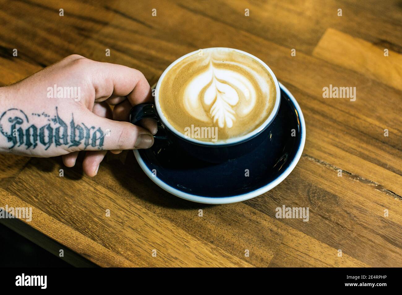 GREAT BRITAIN / England / London/Hand with tatoo holding coffee cup in an indoor cafe in London.Close up of hands holding cup of coffee Stock Photo