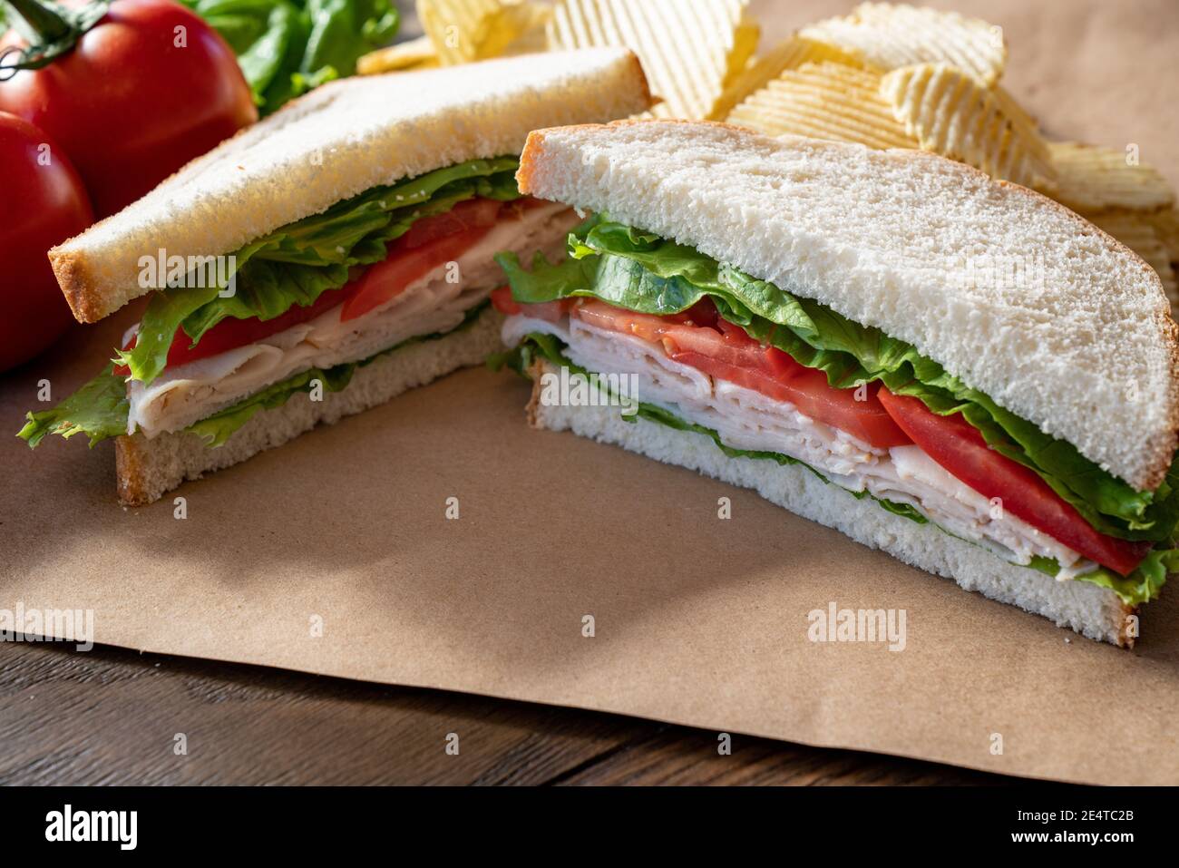 Fresh turkey, lettuce and tomato sandwich cut in half on brown paper Stock Photo