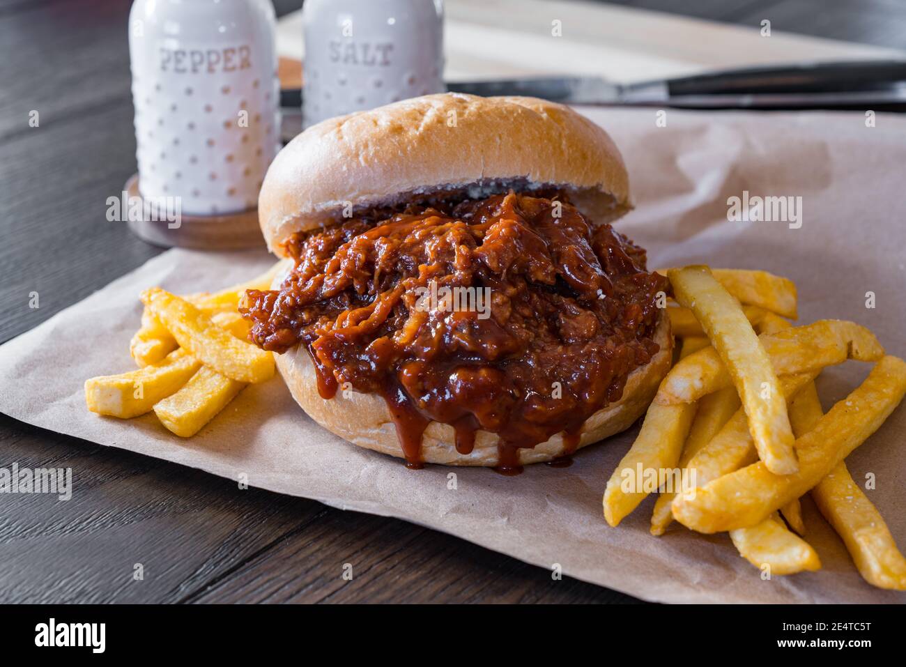 Hot, fresh pulled pork barbecue sandwich with french fried potatoes on brown paper Stock Photo