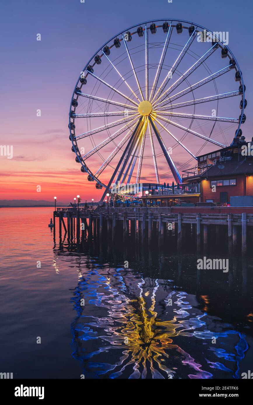 The Seattle Great Wheel rises 175 feet over Pier 57, overlooking the Seattle skyline and Elliott Bay as the sun sets in the west Stock Photo