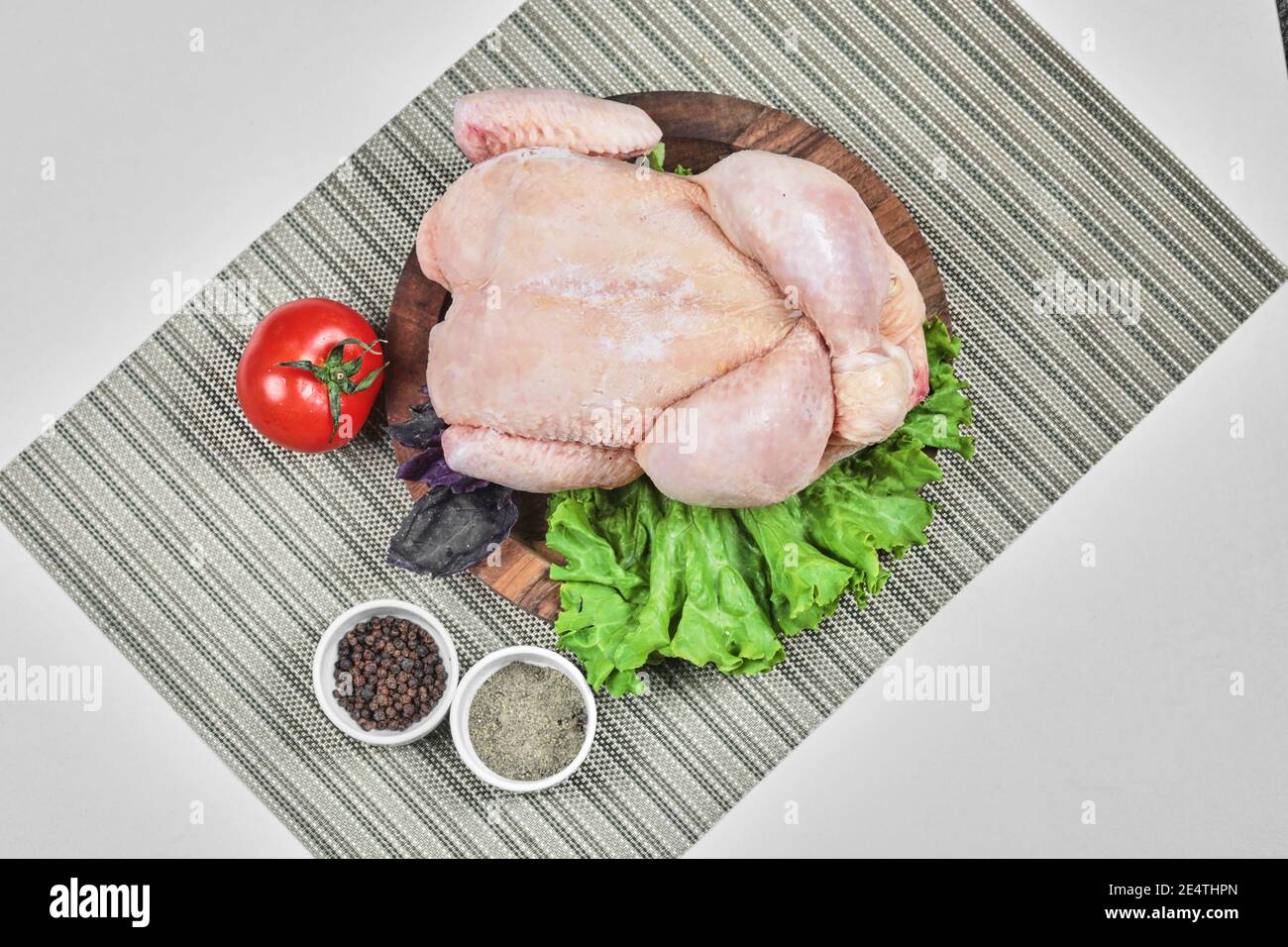Raw whole chicken on wooden plate with lettuce, tomato and spices Stock Photo