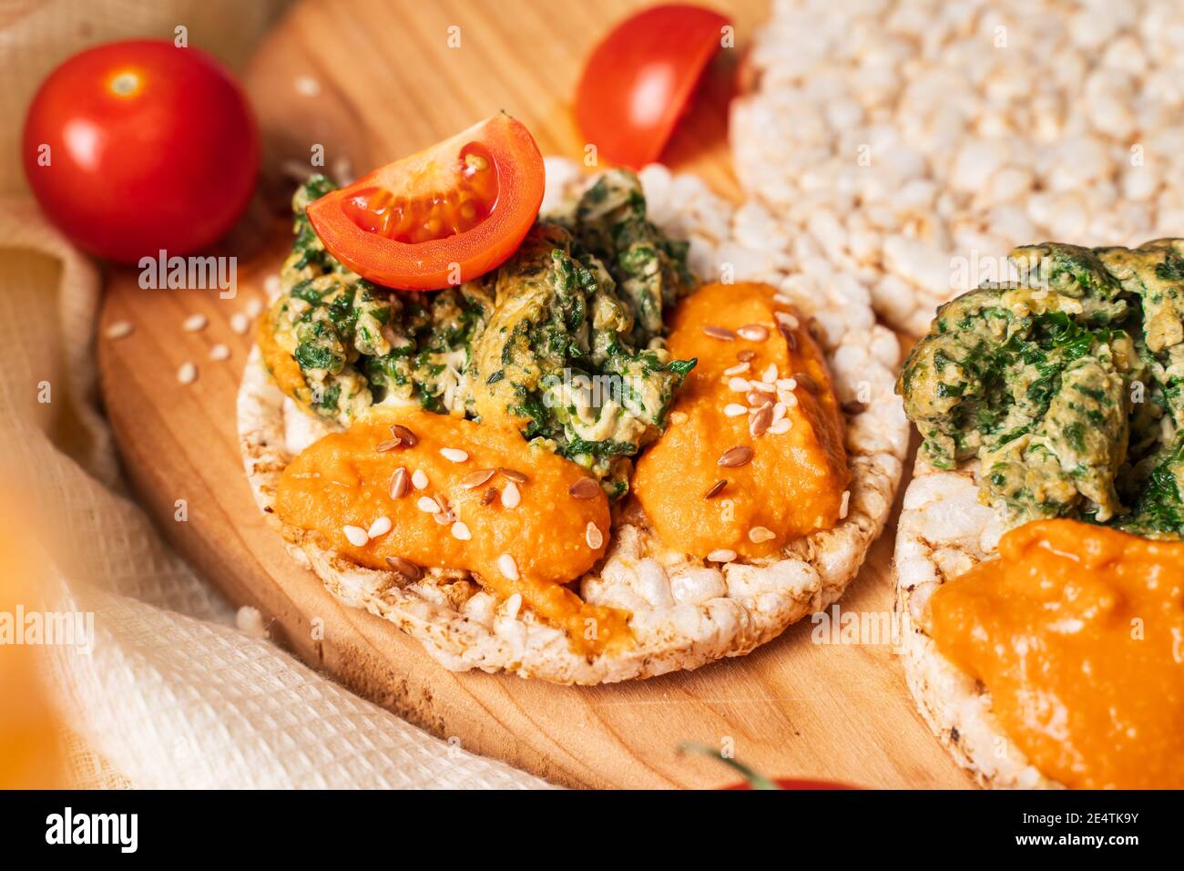 Crispy puffed rice cakes on table with hummus spread spinach with eggs and tomato and vegetables on the table - close up view on healthy vegetarian br Stock Photo