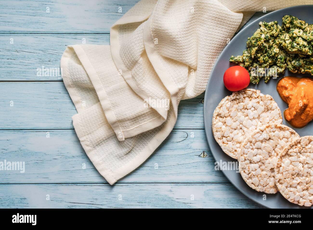 Crispy puffed rice cakes on table with hummus spread spinach with eggs