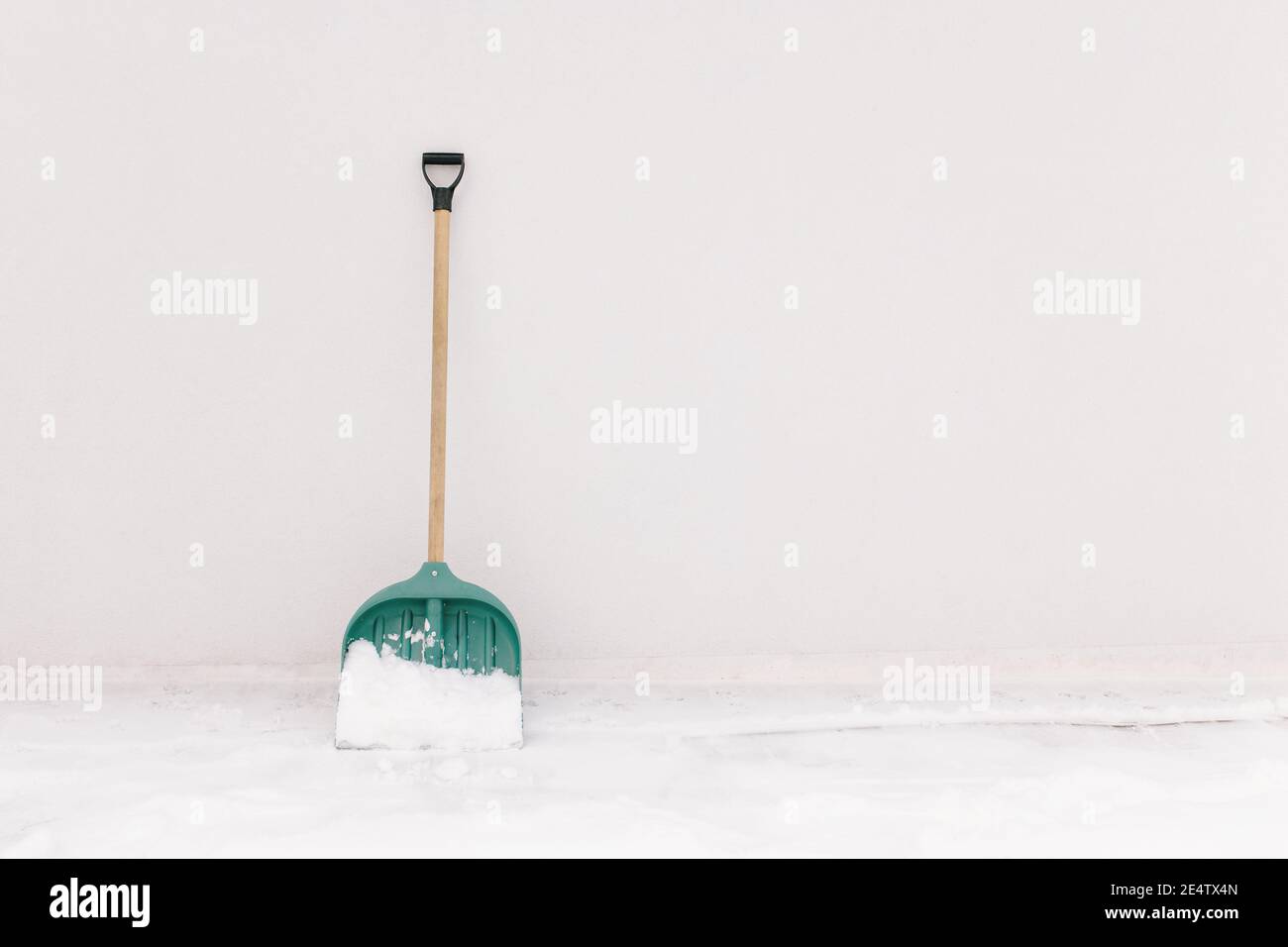 Snow shovel propped against the white wall of the house Stock Photo
