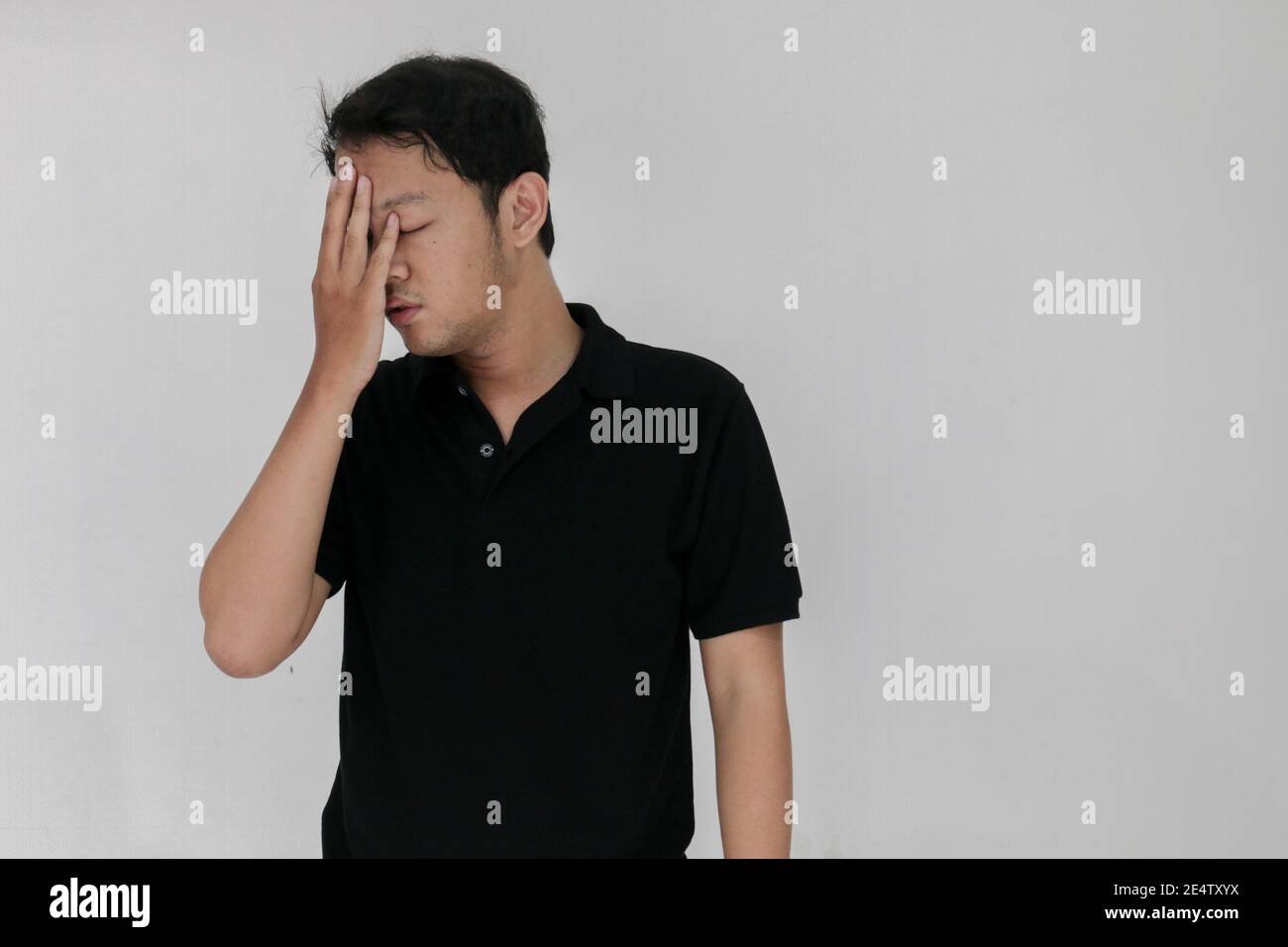Portrait of young asian man isolated on grey background suffering from severe headache, pressing fingers to temples, closing eyes to relieve pain with Stock Photo