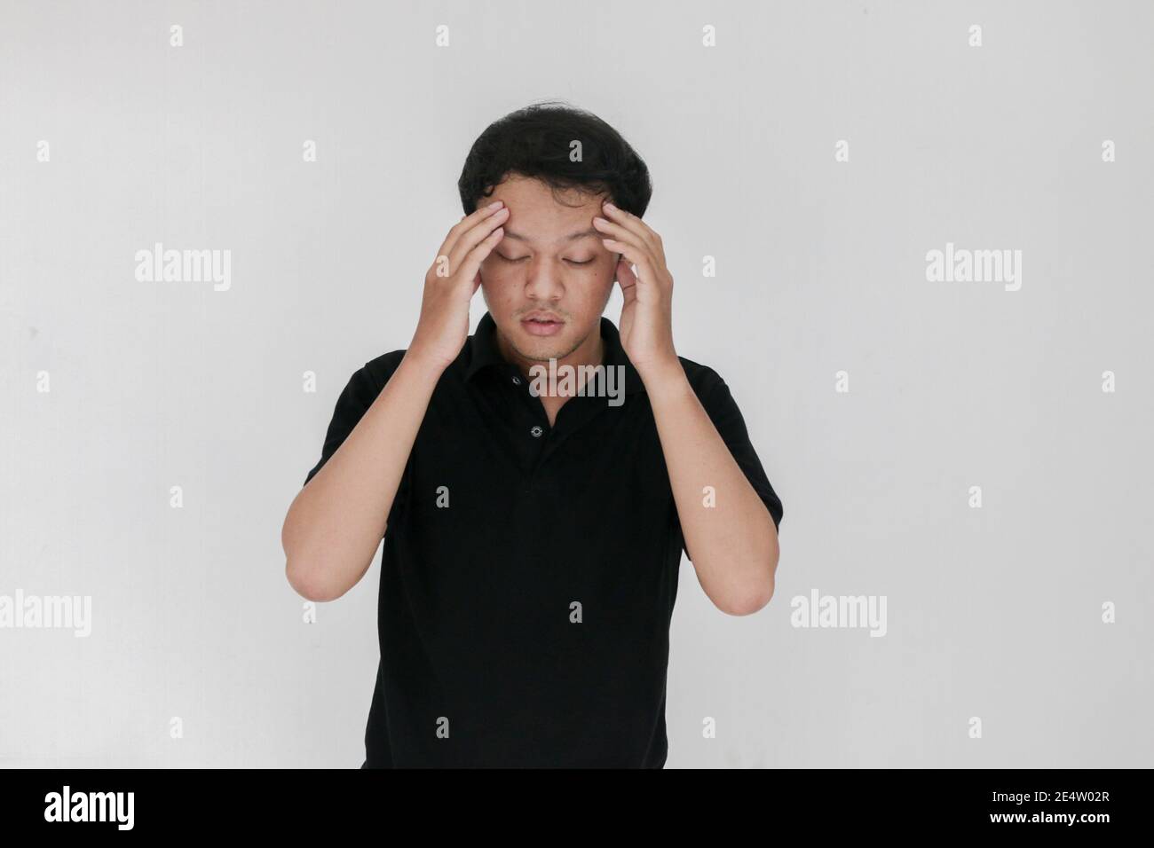 Portrait of young asian man isolated on grey background suffering from severe headache, pressing fingers to temples, closing eyes to relieve pain with Stock Photo