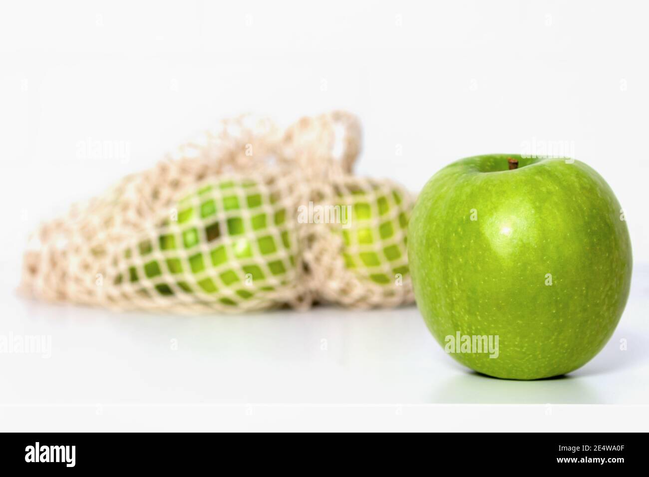Green apples in eco mesh bag on white kitchen table. Market shopping. Food and Environment concept. Zero waste. Close up. Banner. Stock Photo