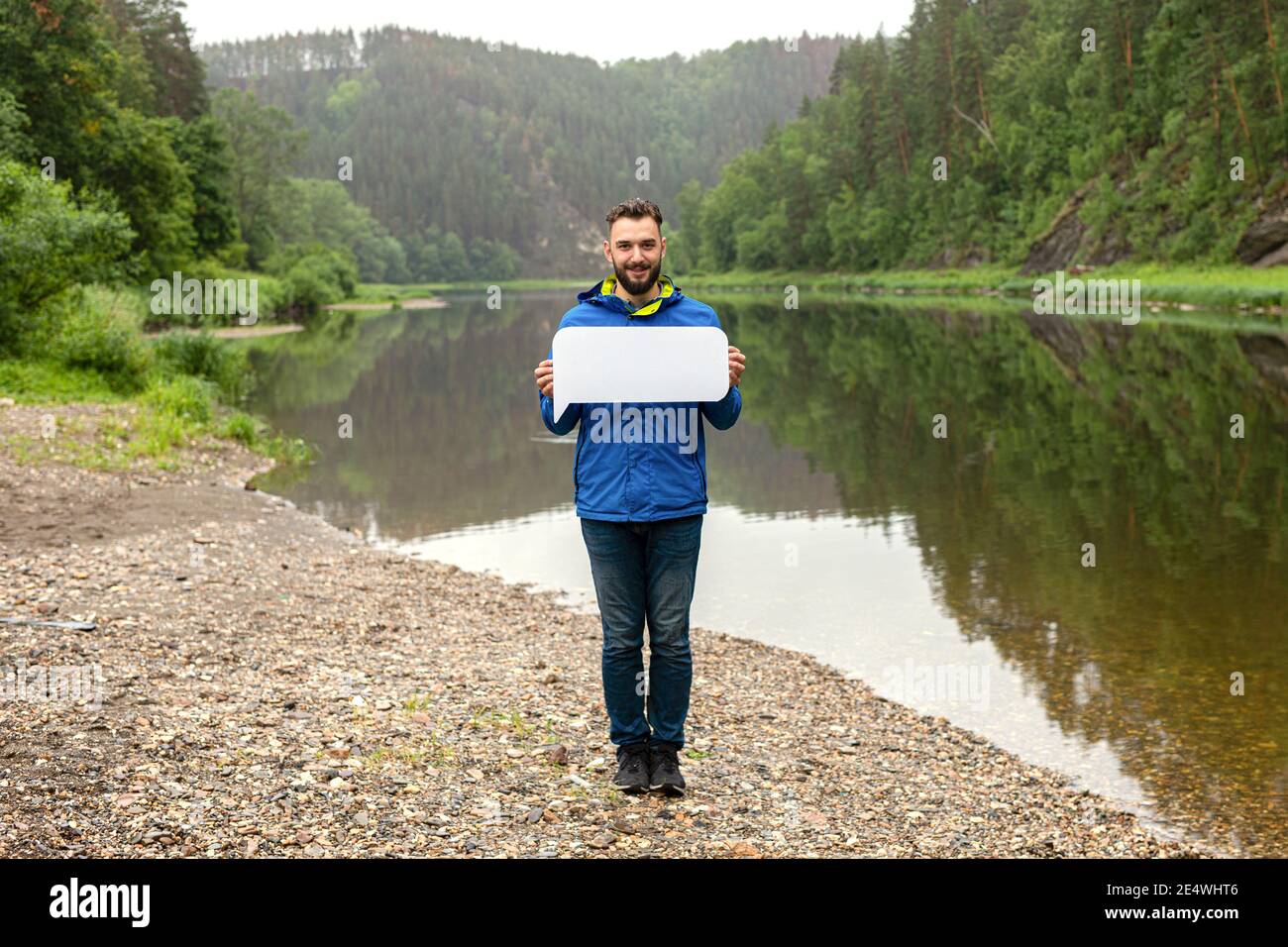 Your text here. Handsome young man holding empty blank board outdoors with beautiful nature on background. Stock Photo