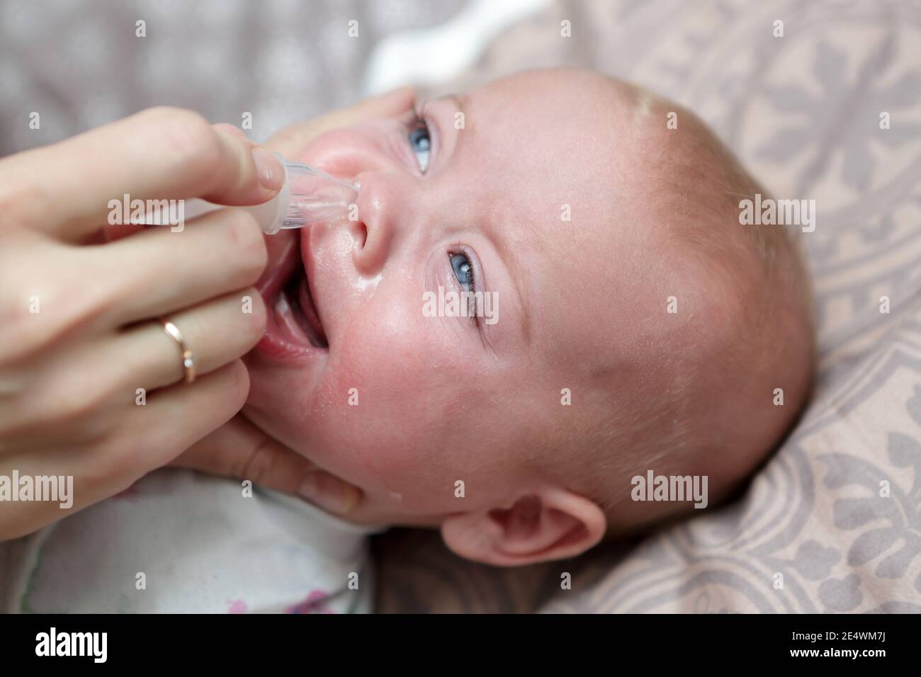 Mother treats her baby with nasal aspirator at home Stock Photo