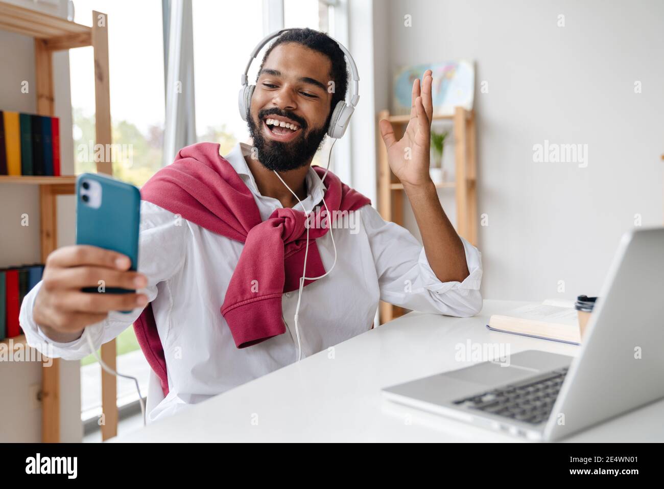 Happy african american guy in headphone using cellphone and waving hand