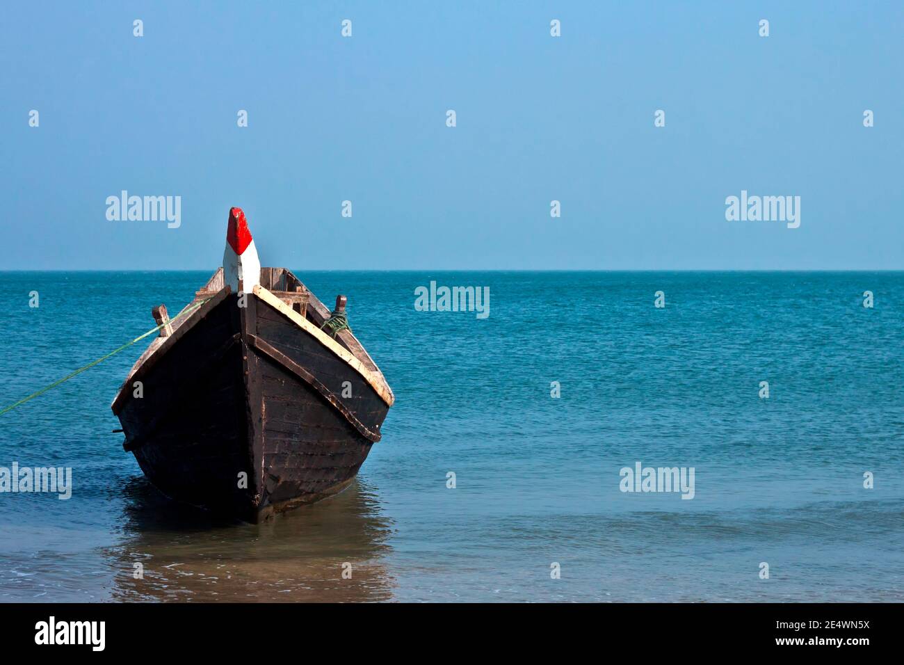 A lone wooden boat floating in the waters of the blue sea. Stock Photo