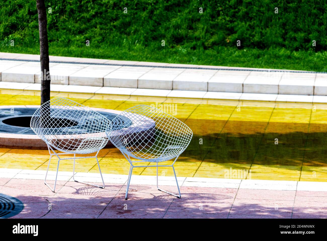 Two wicker chairs made of wire stand near a tree on a tile. Nobody is there unusual chairs are standing in a park Stock Photo Alamy