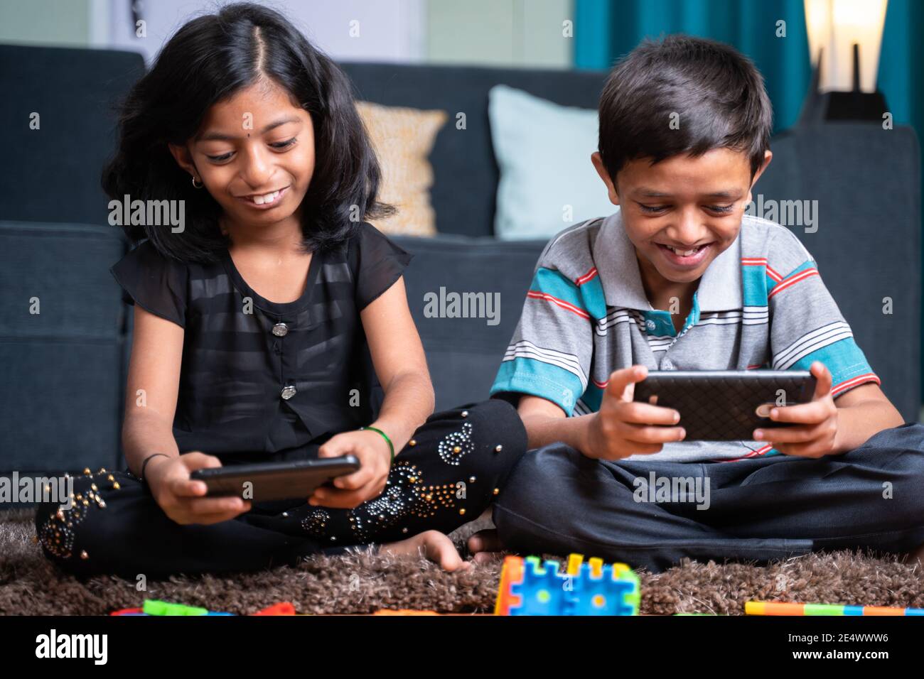 Two young sibling kids playing online video game on mobile phone at home - concept of smartphone game addiction. holidays, modern technology lifestyle Stock Photo