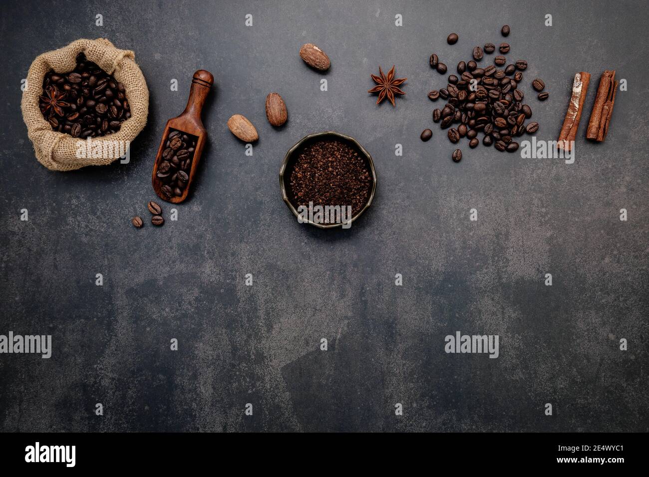 Roasted coffee beans with coffee powder and flavourful ingredients for make tasty coffee setup on dark stone background. Stock Photo