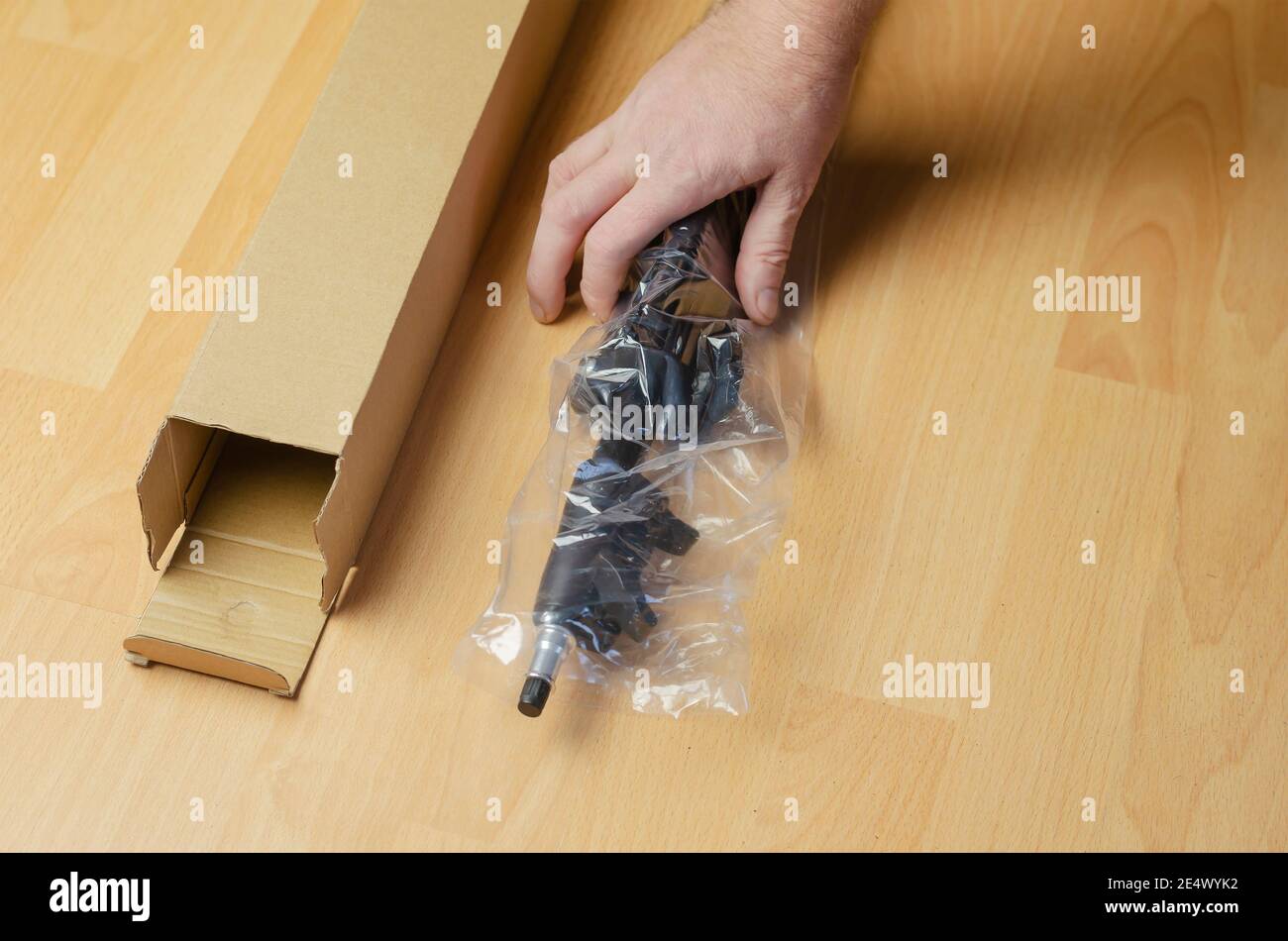 Continuous light photographic equipment, softbox. Hand places a new black softbox tripod in clear packaging next to the cardboard box. Stock Photo