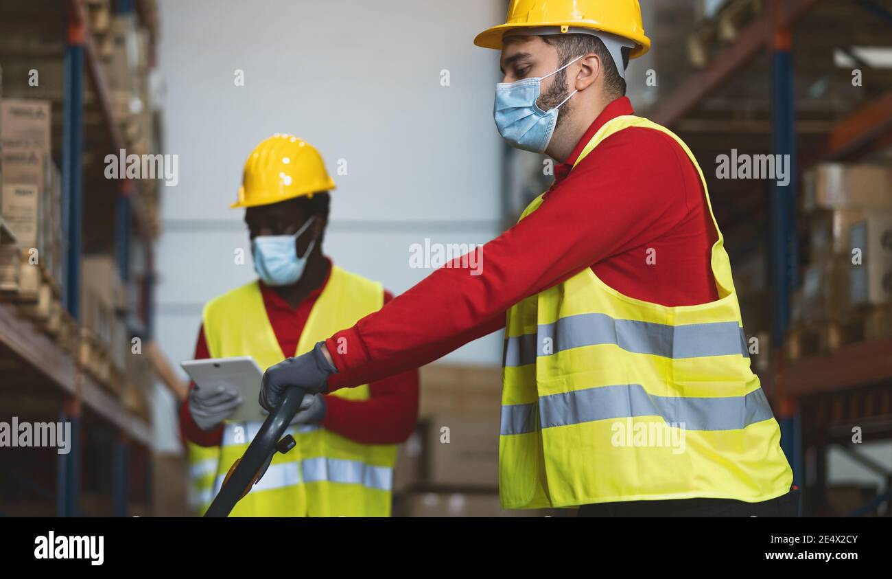Team working in warehouse doing inventory using digital tablet loading delivery boxes while wearing face mask during corona virus pandemic Stock Photo