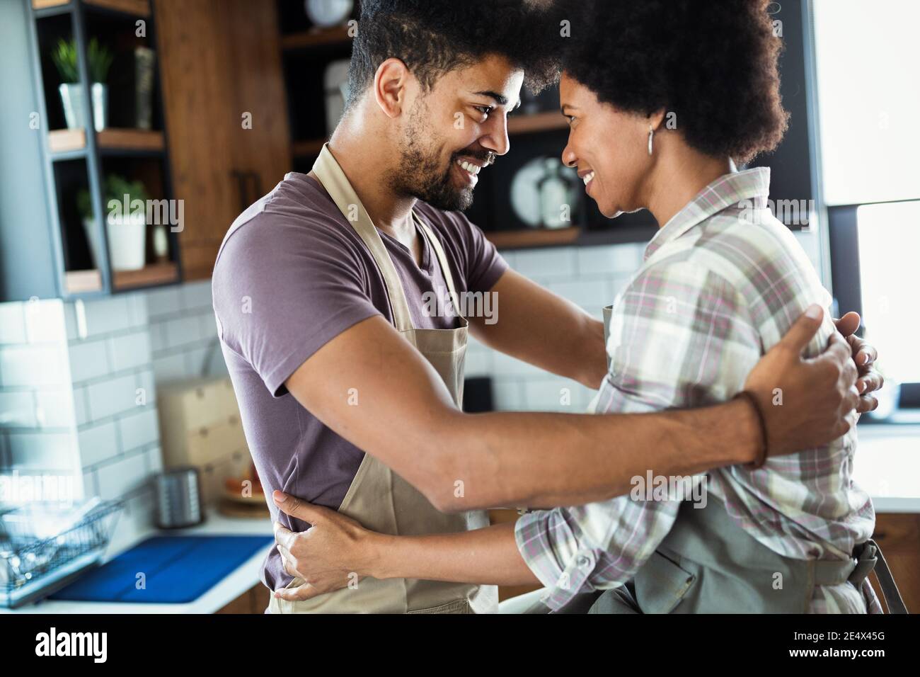 Beautiful couple are hugging and smiling while spending time in kitchen ...