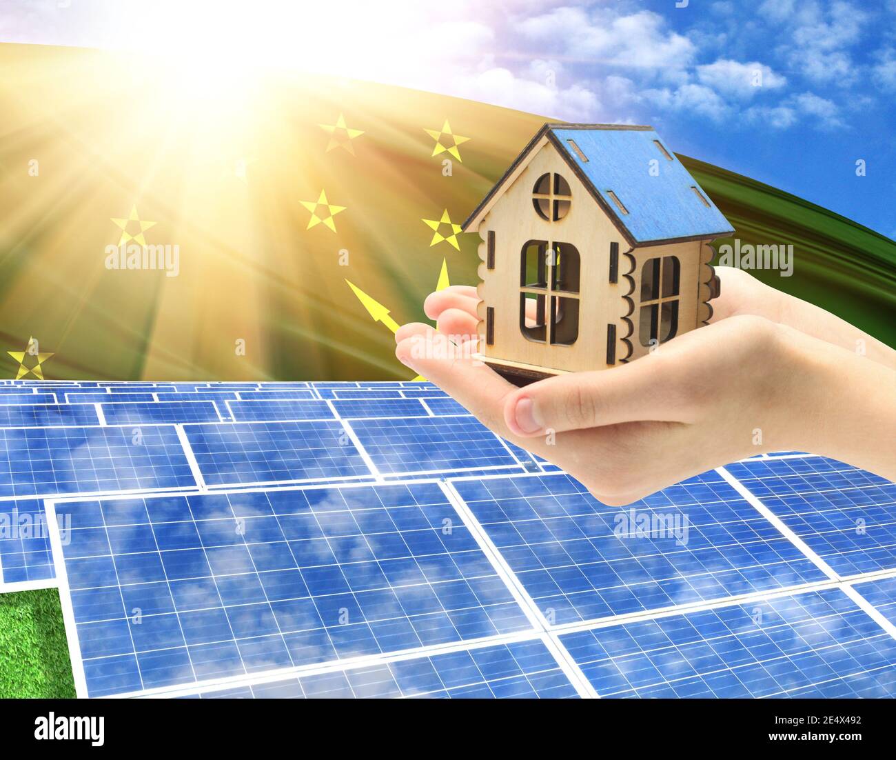 The photo with solar panels and a woman's palm holding a toy house shows the flag of Adygea in the sun. Stock Photo